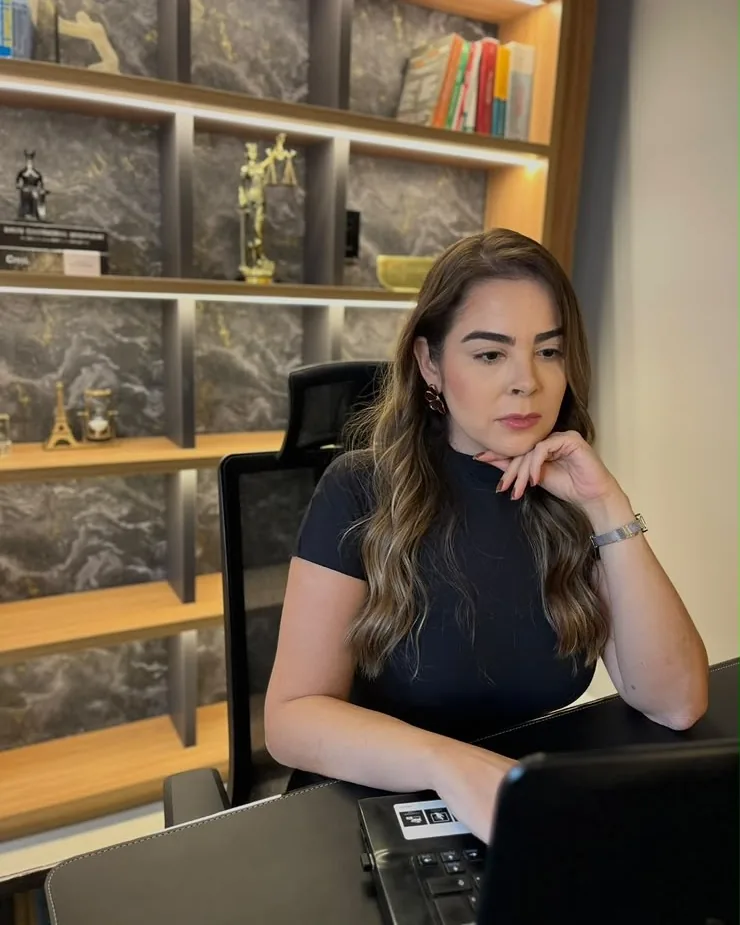 Dra. Fabiana concentrada, analisando documentos no computador em sua mesa de trabalho