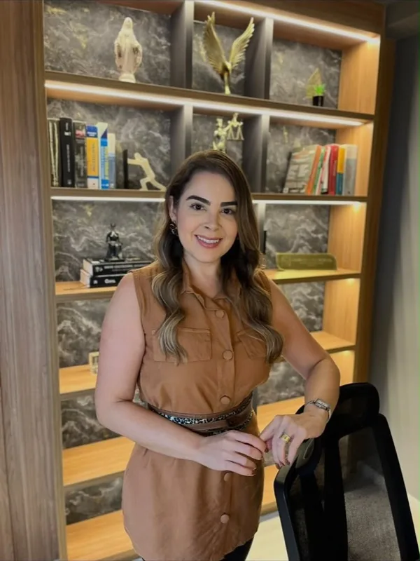 Dra. Fabiana em pé no escritório, diante da estante com livros e a estátua da Justiça